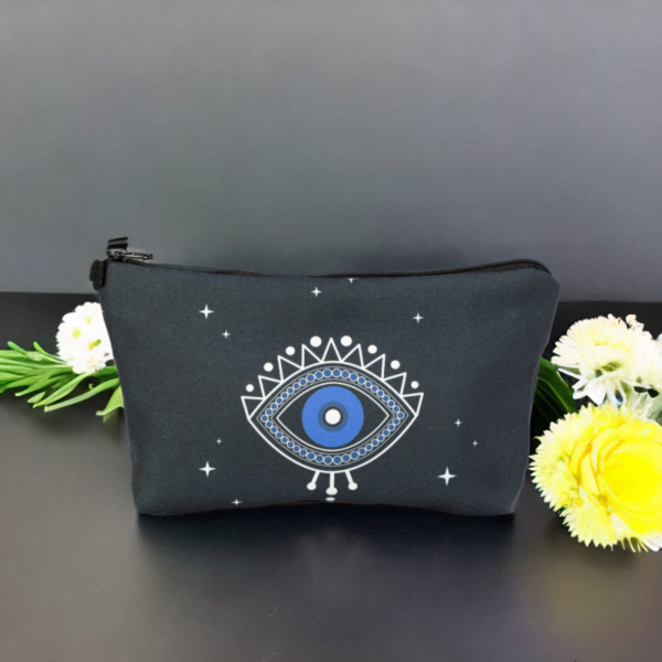 A black star bag with blue evil eye styling sitting on a black top surrounded by flowers.