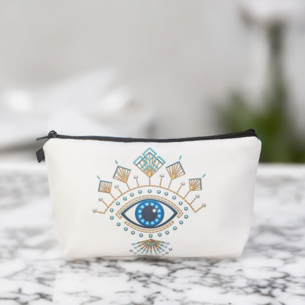 The Roula bag, a white cosmetic bag with artistic blue and gold evil eye pattern.