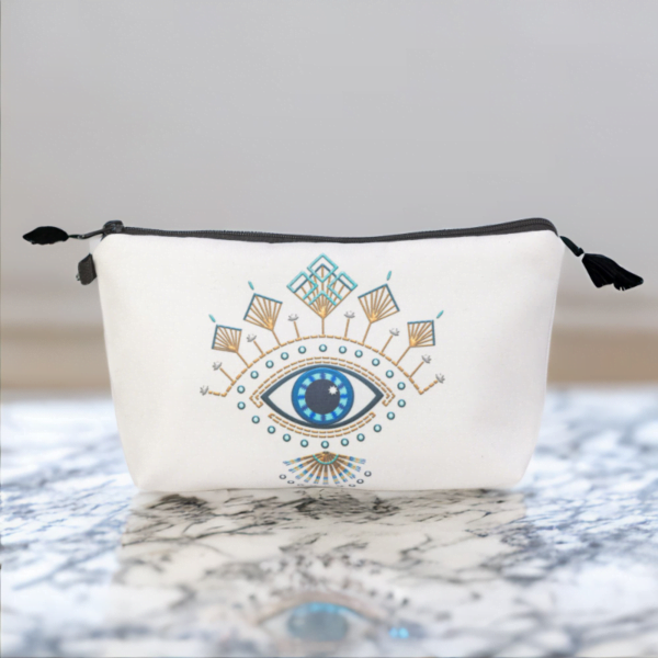 The Roula bag, a white cosmetic bag with artistic blue and gold evil eye pattern on a marble table.