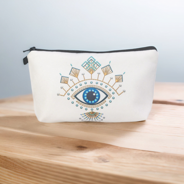 The Roula bag, a white cosmetic bag with artistic blue and gold evil eye pattern on a wooden top.