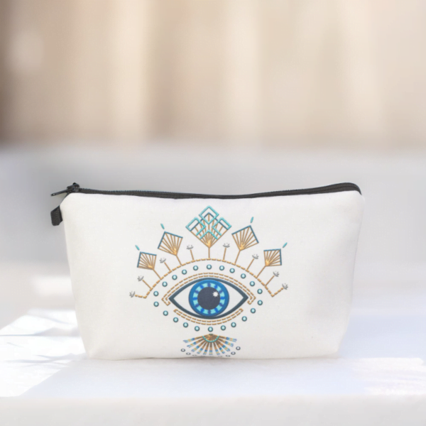 The Roula bag, a white cosmetic bag with artistic blue and gold evil eye pattern on a marble top.