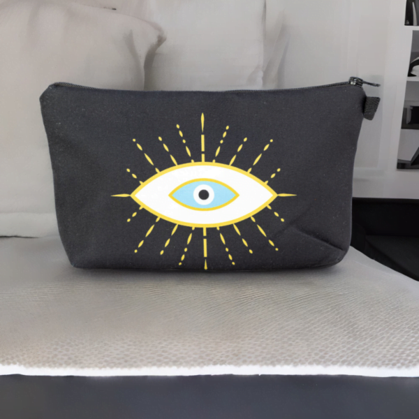 The alma bag, a black cosmetic bag with white and gold evil eye pattern on a bed.