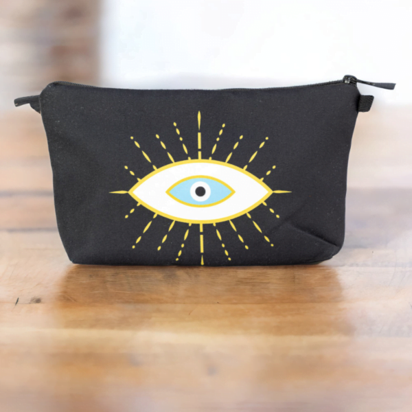 The alma bag, a black cosmetic bag with white and gold evil eye pattern on a wooden surface.