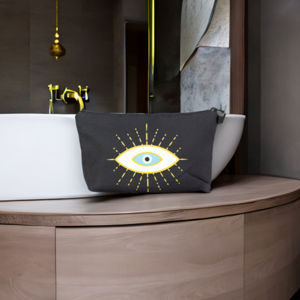 The alma bag, a black cosmetic bag with white and gold evil eye pattern in front of a bathtub.
