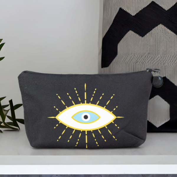 The alma bag, a black cosmetic bag with white and gold evil eye pattern on a white surface.