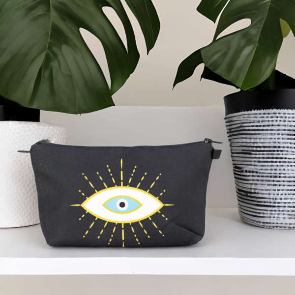 The alma bag, a black cosmetic bag with white and gold evil eye pattern on a shelf with a potted plant.