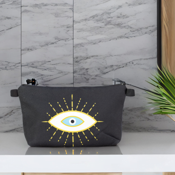 The alma bag, a black cosmetic bag with white and gold evil eye pattern on a table next to a potted plant.
