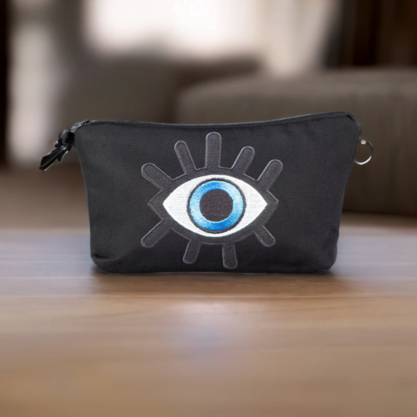 The alia bag, a black cosmetic bag with an artistic blue and black evil eye image in the centre on a wooden top.