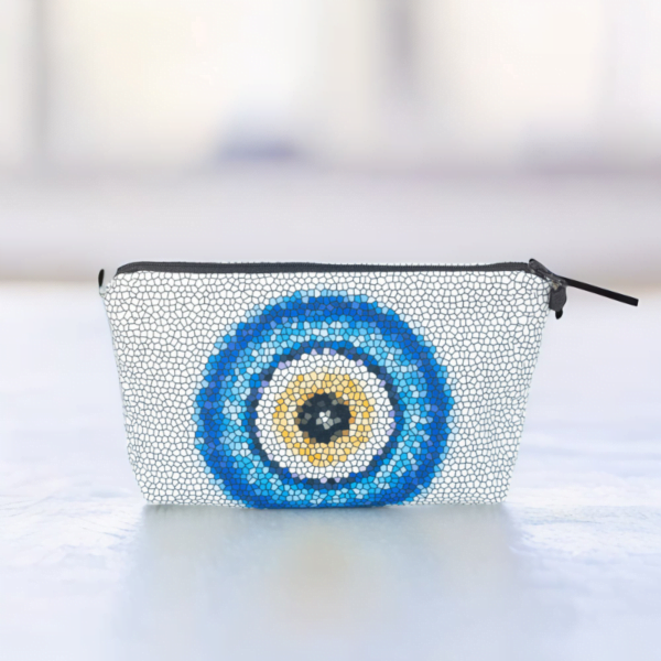 The Nadine cosmetic bag, a white mosaic patterned bag adorned with large blue and yellow evil eye motif in the centre on a white surface.