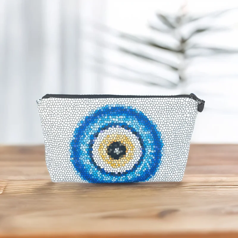 The Nadine bag, a white mosaic patterned cosmetic bag adorned with large blue and yellow evil eye motif in the centre