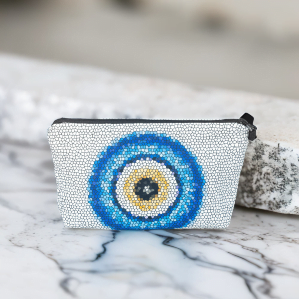 The Nadine bag, a white mosaic patterned bag adorned with large blue and yellow evil eye motif in the centre siting on a marble top.
