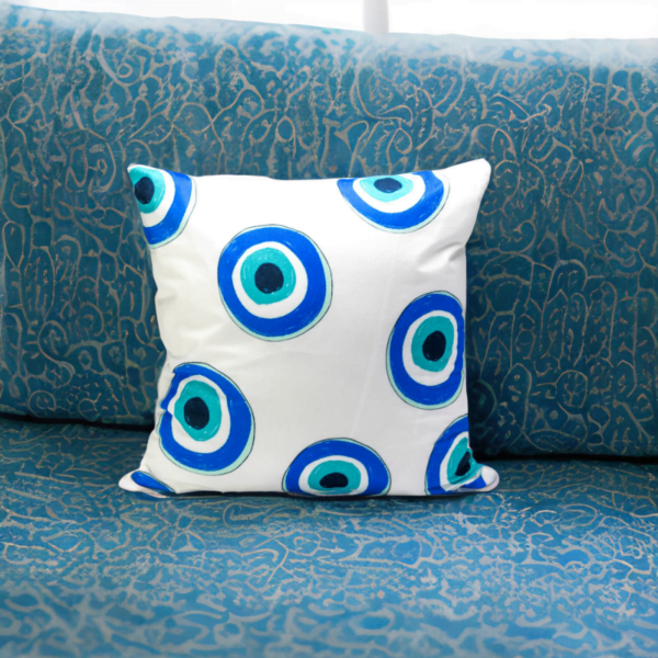 Malda Cushion, a white and plump cushion adorned with blue and white evil eye imagery on a blue couch.