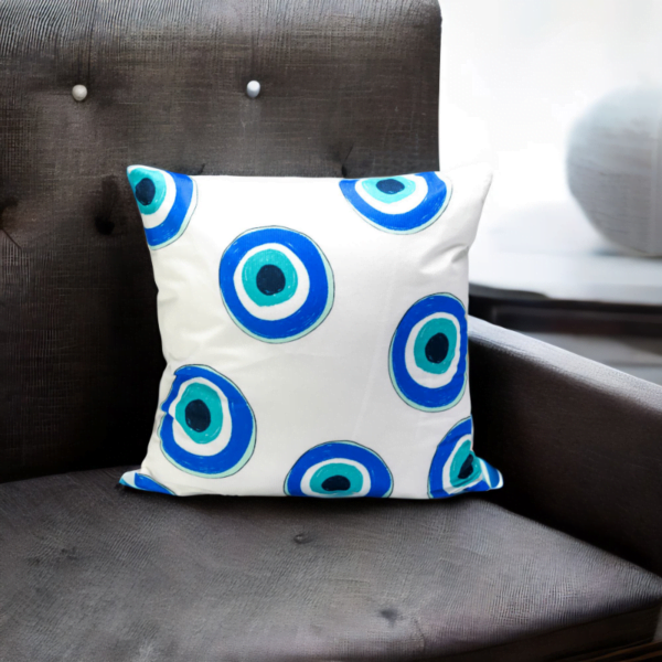 Malda Cushion, a white and plump cushion adorned with blue and white evil eye imagery on a dark chair.