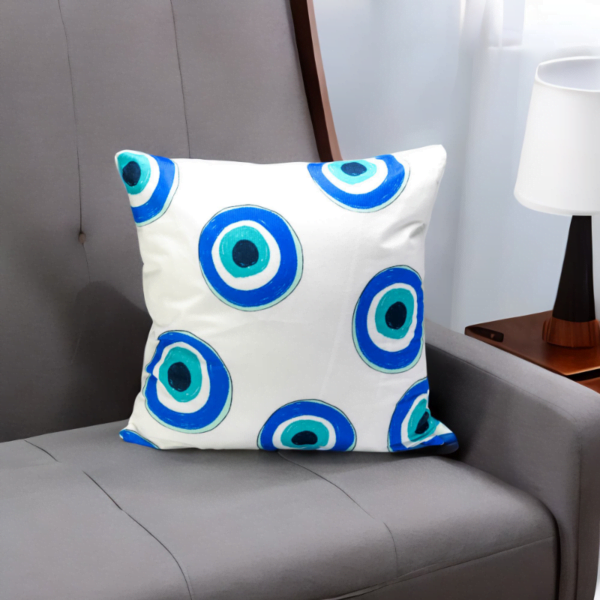 Malda Cushion, a white and plump cushion adorned with blue and white evil eye imagery on a sofa.