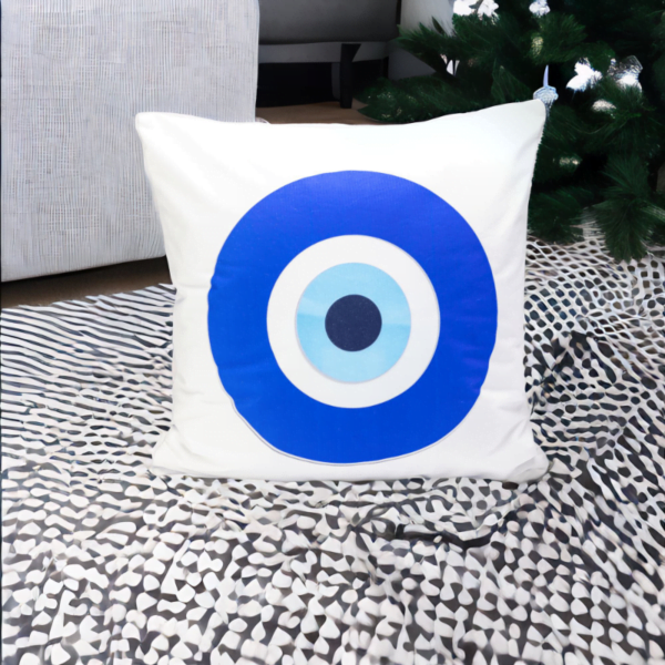 the hiba cushion, a white and plump cushion adorned with artistic blue and white evil eye imagery on a rug.