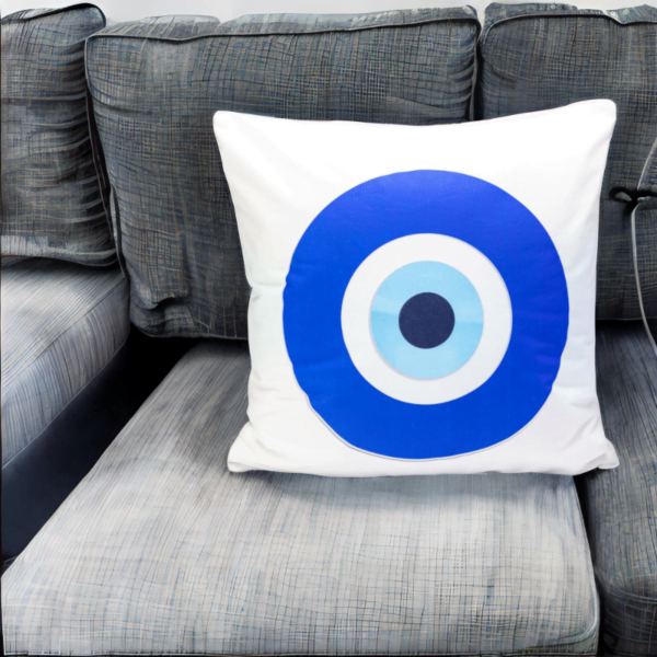 the hiba cushion, a white and plump cushion adorned with artistic blue and white evil eye imagery on a grey sofa.