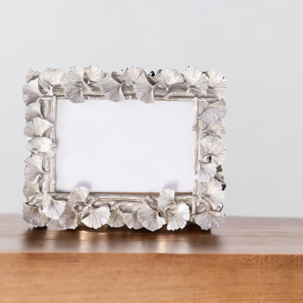 A silver ginkgo leaf landscape frame on a wood table.
