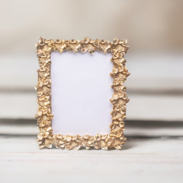 A handmade gold photo frame with leaf designs, placed on a wooden table in London.