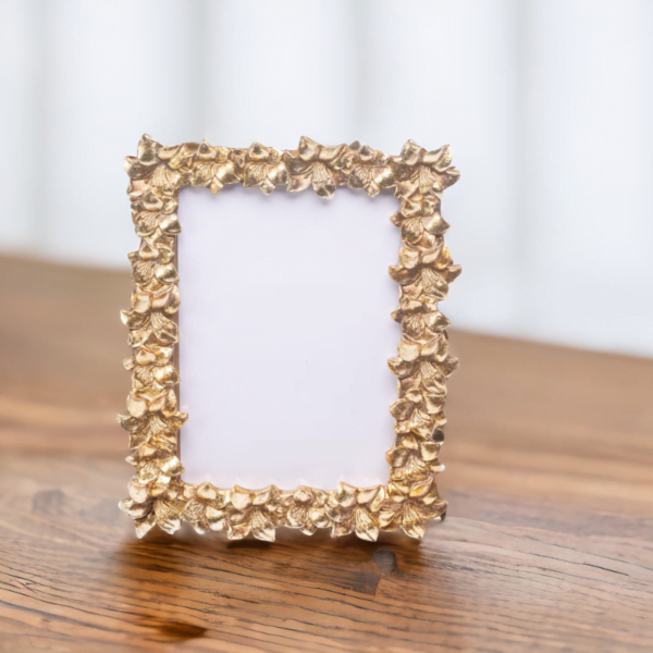 A handmade gold photo frame with leaf designs, placed on a wooden table in London.