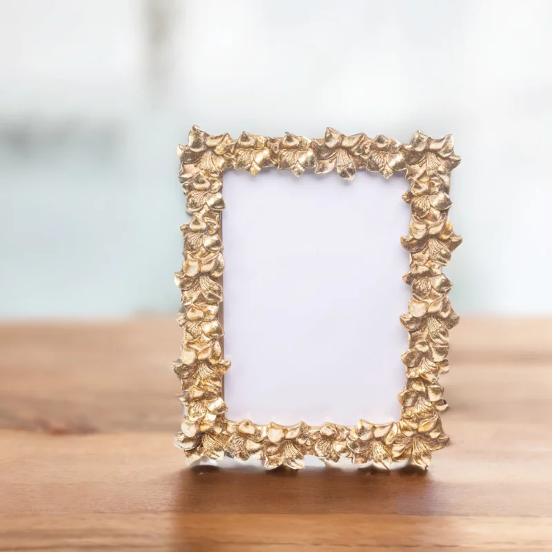 A handmade gold photo frame with leaf designs, placed on a wooden table in London.