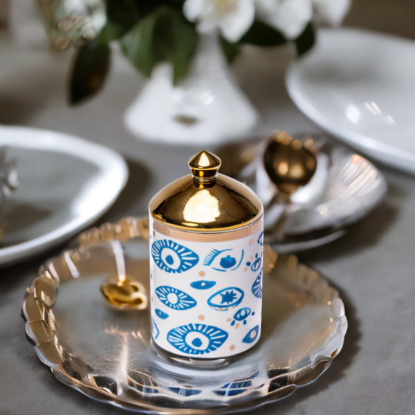 a decorative canister in blue and white with gold accents and evil eye styling on a silver plate.