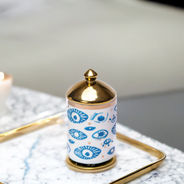 a decorative canister in blue and white with gold accents and evil eye styling on a marble tray.
