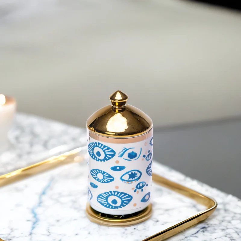 a decorative canister in blue and white with gold accents and evil eye styling on a marble tray.