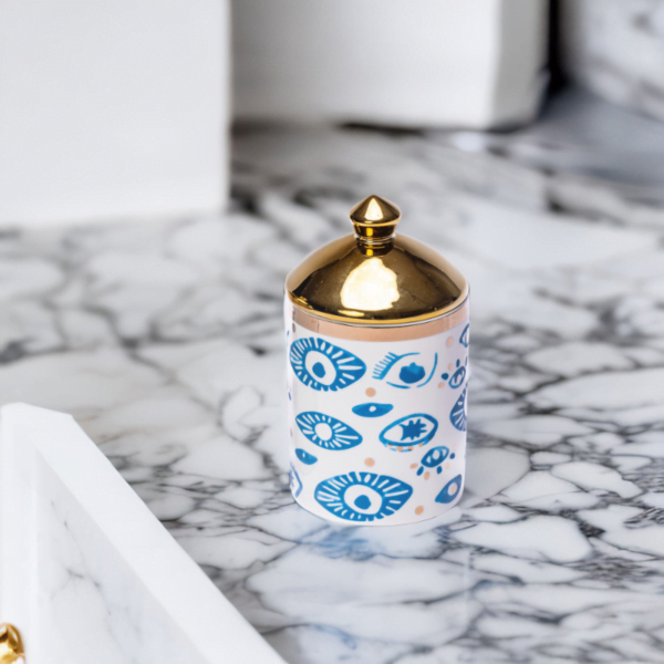 a decorative canister in blue and white with gold accents and evil eye styling on a marble top.