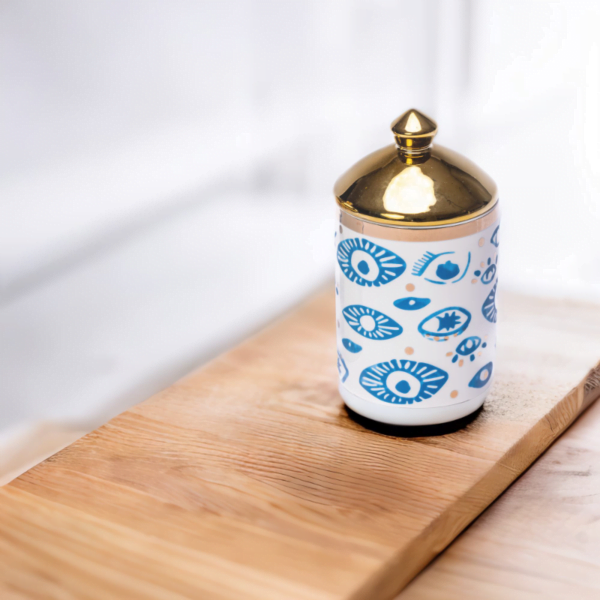 a decorative canister in blue and white with gold accents and evil eye styling on a wooden table.