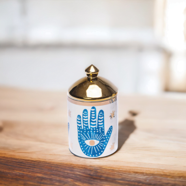 a blue and white porcelain canister with gold lid and Hamsa hand styling on a wooden top.
