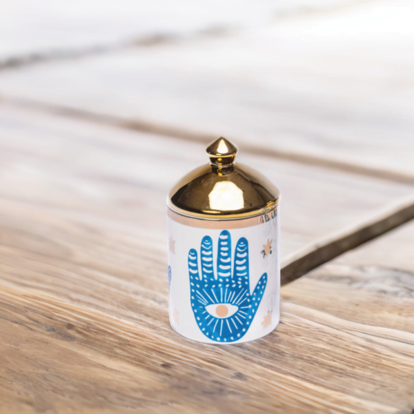a blue and white porcelain canister with gold lid and Hamsa hand styling on a table.