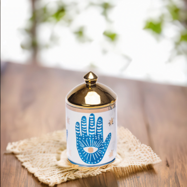 a blue and white porcelain canister with gold lid and Hamsa hand styling on coaster.