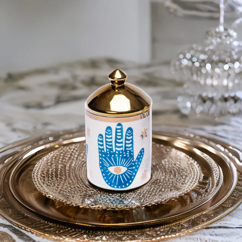 a blue and white porcelain canister with gold lid and Hamsa hand styling on a table.