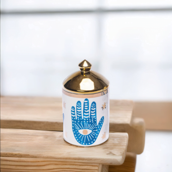 a blue and white porcelain canister with gold lid and Hamsa hand styling on a wooden table.