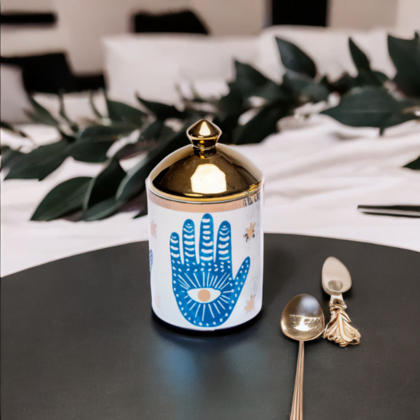 a blue and white porcelain canister with gold lid and Hamsa hand styling on a round wooden tray.