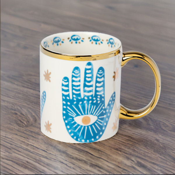 A blue and white Hamsa Hand Mug with gold accents on wooden table.