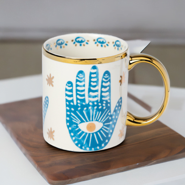 A blue and white Hamsa Hand Mug with gold accents on wooden coaster.