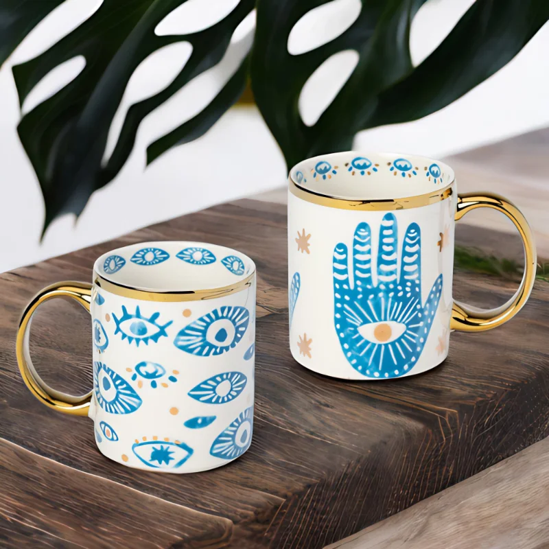 Hamsa Hand and Evil Eye mugs on a wooden table.