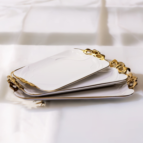 Three white and gold Flat Ceramic Serving Plates on a white table.