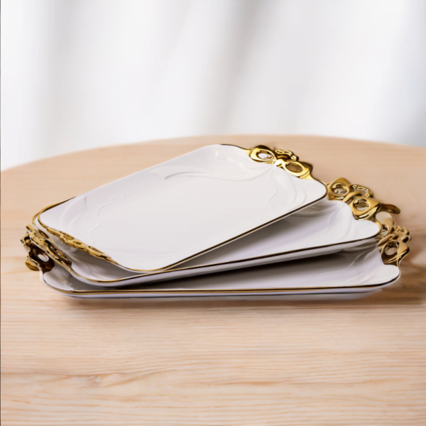 Three flat ceramic serving plates with gold handles on a wooden table.