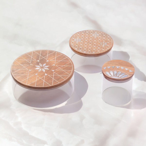 A set of three round storage containers made with transparent acrylic and a wooden lid adorned with quality mother of pearl inlay for a touch of artistic brilliance.