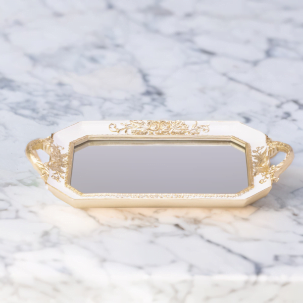 A white octagon tray with a mirror bottom and gold accents on a marble top.