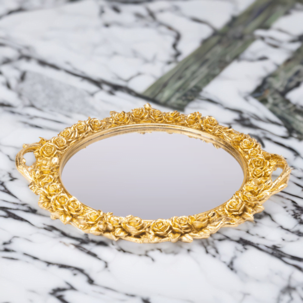 An ornate round gold tray with mirror bottom and gold flower styling on a marble top.