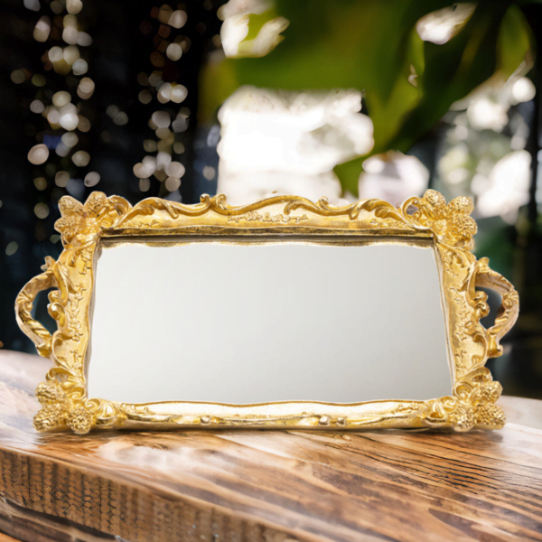 An ornate golden Tray (Rahaf Tray) with mirror bottom on top of a wooden table.