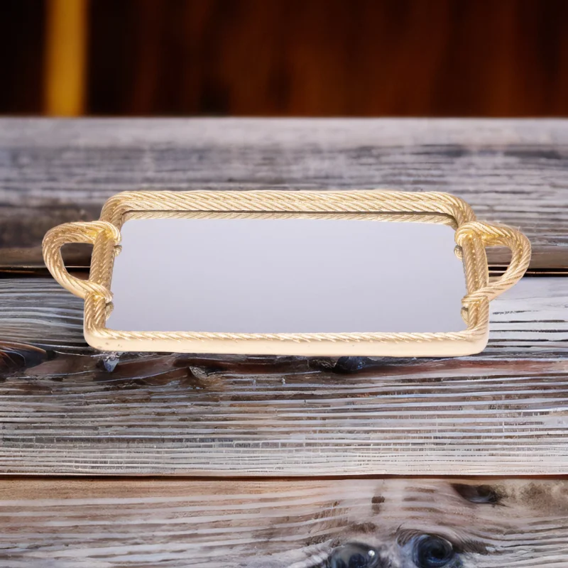 A gold mirror tray with twisted metal styling on a wooden table.