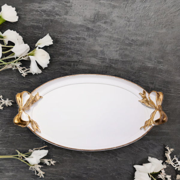 A white tray with gold accents and ribbon handles on a wood surface.