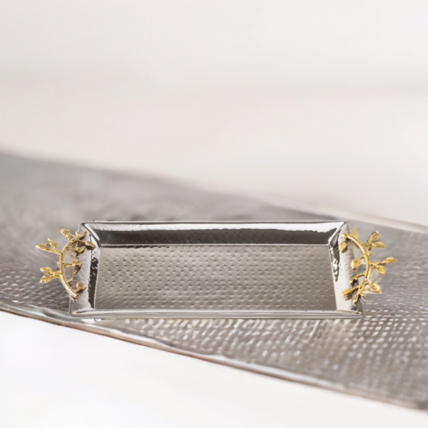 Stainless steel rectangle serving tray with hammered styling and gold accented handles on a table.