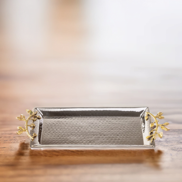 Stainless steel serving tray with hammered styling and gold accented handles on a light wooden table.