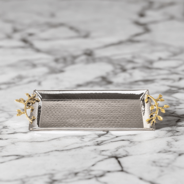 Stainless steel serving tray with hammered styling and gold accented handles on a marble table.