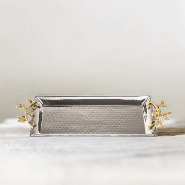 Stainless steel rectangle serving tray with hammered styling and gold accented handles on a marble table.